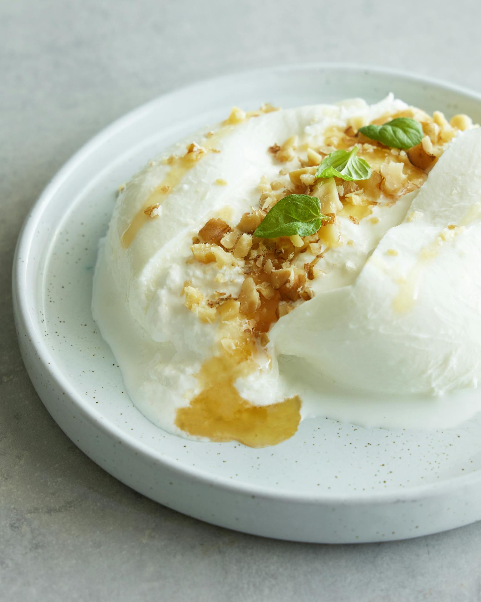 Close-up of creamy burrata cheese topped with honey and nuts on a white plate.